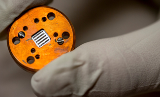 gloved hand holding a chip used to detect gravitational waves