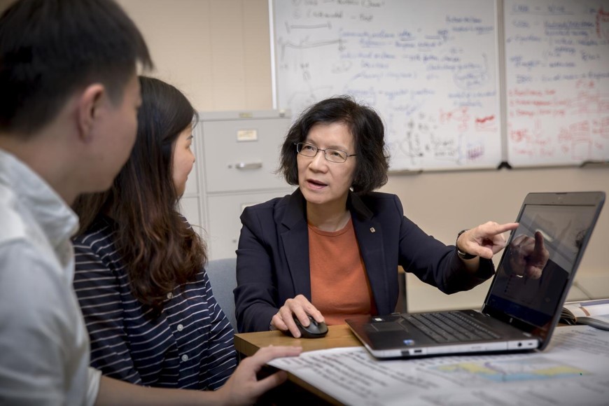 A professor sits at a computer with two students