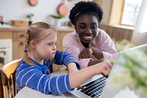 Photo of a teacher working with a girl with downs syndrome on computer use.