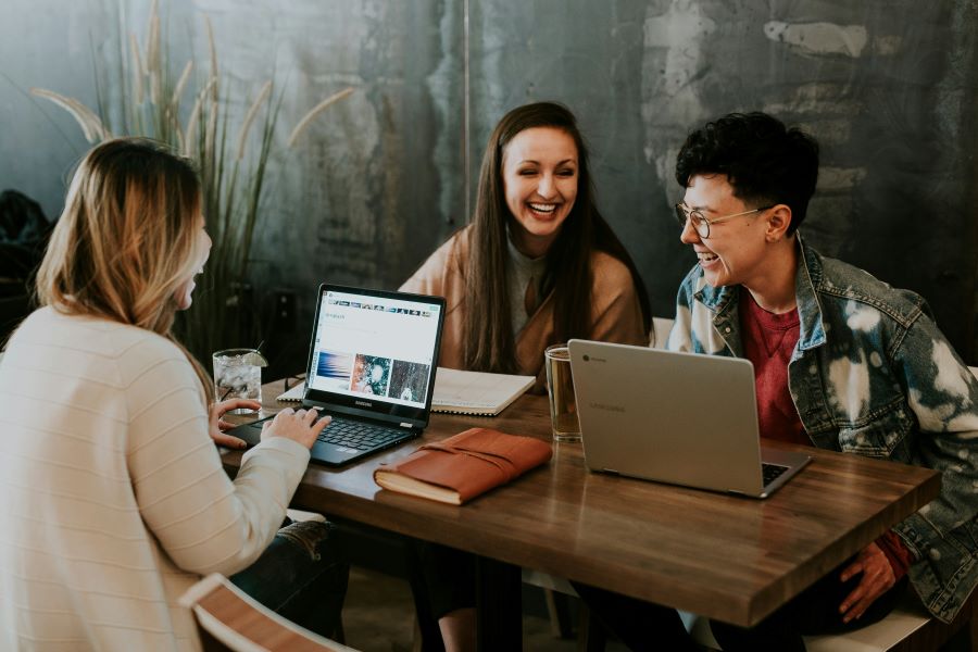 Three students sitting at table with laptop laughing