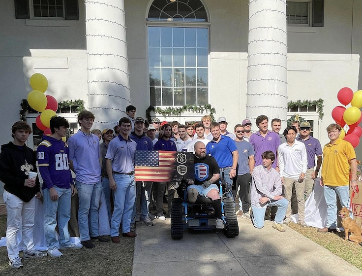 kappa alpha order members presenting a veteran with all-terrain track chair